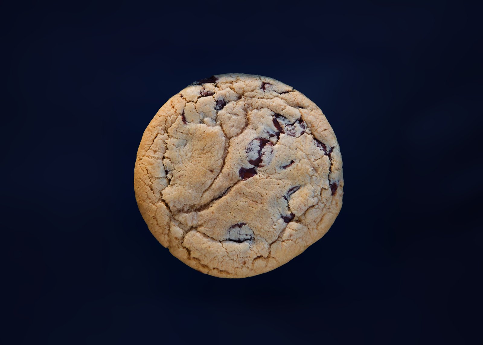 A chocolate chip cookie seen from above against a dark blue backdrop