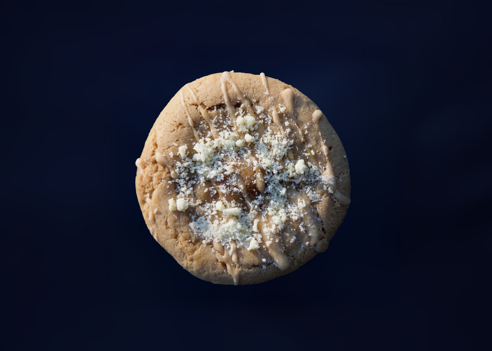 A glazed cookie scattered with white chocolate crumble against a dark blue backdrop